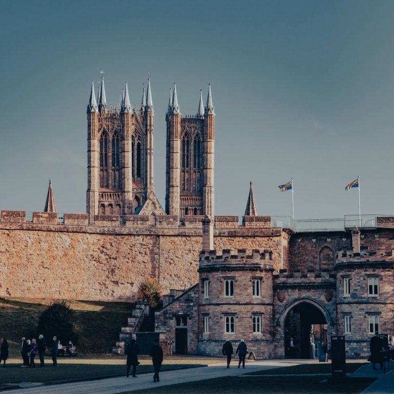 blood-tests-in-lincoln Historic castle with tall towers, stone walls, and flags flying, set against a blue sky.